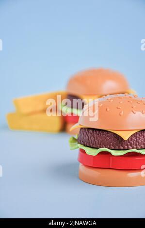 Plastic childrens toy burger with salad, tomato, meat and French fries on blue. Concept of harmful artificial food. Unhealthy. Not organic. Not useful Stock Photo
