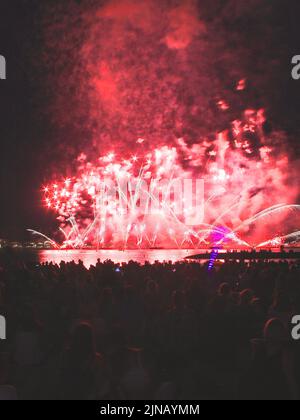 Red fireworks exploding ina smoky evening on the sea with people watching at them Stock Photo