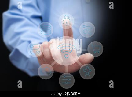 a man in a blue shirt on a dark background presses virtual buttons with symbols of cloud storage, data protection, online shopping and other modern te Stock Photo