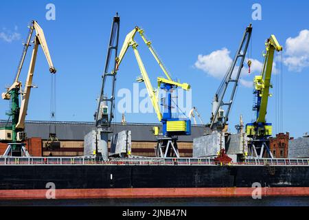 Yellow and blue painted cranes are loading bulk carriers in the port against a blue sky background Stock Photo