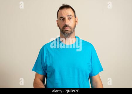 Isolated photo of handsome man with fashionable beard, mustache and hairstyle, wears casual blue t-shirt, poses in studio on beige background. Stock Photo