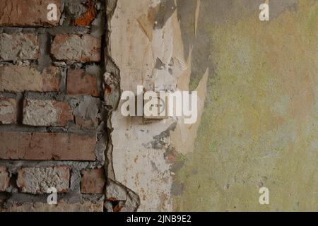Old wall with a socket under renovation. Brickwork and old plaster without wallpaper. The textured background of a vintage wall. Abstract background with construction concept. Stock Photo
