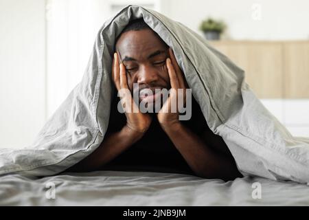 Sleepy Black Guy Covered With Blanket Lying In Bedroom Stock Photo