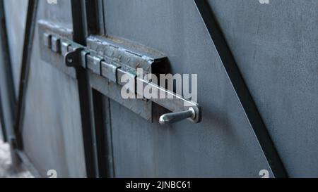 Old gray metal gate with a deadbolt. Shiny polished bolt handle close-up. Traces of corrosion on metal. Aging process. rusty surface. Home security. Outdoors. Stock Photo