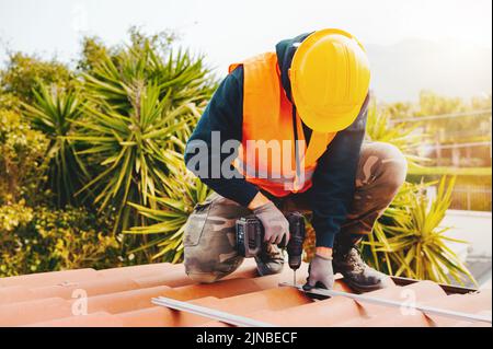 Technical worker works with drill on the roof of a house Stock Photo