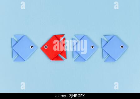 Red paper fish swimming swimming against the current in opposite direction of blue fish Stock Photo