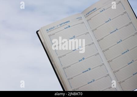 Close-up of the blank pages of a planner that is printed in French, English, Spanish, Italian and German with the cloudy sky in the background Stock Photo