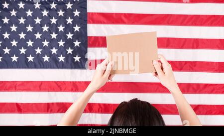 Woman is holding an empty cardboard with Space for Text sign US flag on background. Protest against anti abortion law. Women's strike. Womens rights Stock Photo