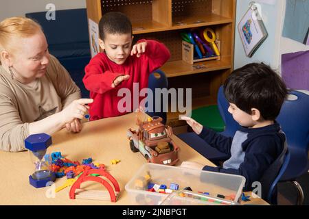 Education Preschool 3 year olds two boys conflict over toy, teacher working with children to resolve conflict, teacher restates problem #4 in series Stock Photo