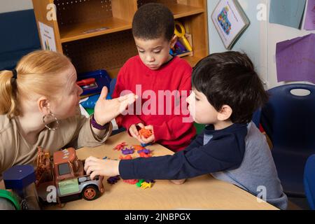 Education Preschool 3 year olds two boys conflict over toy, teacher working with children to resolve conflict, teacher restates problem #3 in series Stock Photo