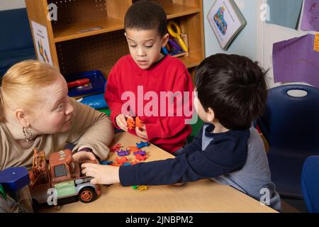 Education Preschool Child Care 3 year olds two boys conflict over toy, teacher working with children to resolve conflict, teacher listens restates pro Stock Photo