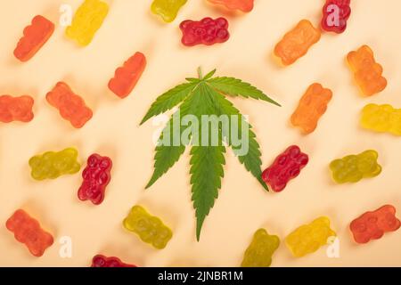 cannabis jelly candies, marijuana multicolored sweets drugs and green leaf on yellow background. Stock Photo
