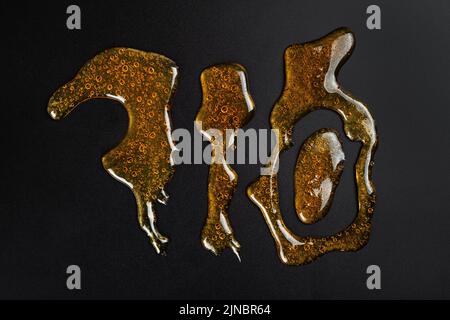 710 lettering golden cannabis wax resin on dark background. Stock Photo