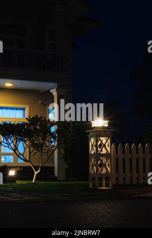 Vertical night photo. Villa fashionable modern Cottage house floors roof large window, shined lantern beams of light, lawn gate Stock Photo