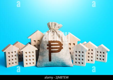 Philippine peso money bag among town houses figurines. Rental business. Municipal budgeting. Rich city. Realtor services. Sale of real estate. propert Stock Photo