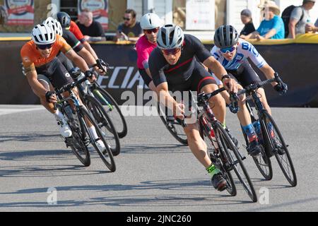 Bicycle racers in the peloton riding a lap of the Criterium, a fast cycling race where the cyclists ride their bikes around a circuit on city streets. Stock Photo