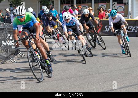 Bicycle racers in a peloton riding a lap of the Criterium, a fast bike race where the cyclists ride their bicycles around a circuit on city roads Stock Photo