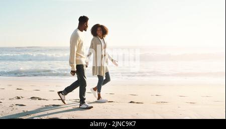 Strolls on the beach with my better half. Full length shot of an affectionate young couple taking a stroll on the beach at sunset. Stock Photo