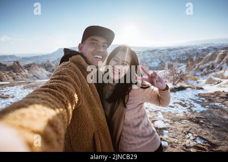 couple taking selfie using smartphone with a beautiful snow landscape Stock Photo