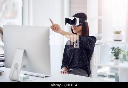 Her business knows no bounds. a young businesswoman wearing a VR headset while working in her office. Stock Photo