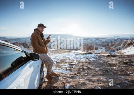man using his mobile phone at the top of the hill while leaning against his car Stock Photo