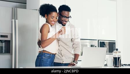 Those look really amazing. a cheerful young couple using a laptop together in the kitchen at home. Stock Photo