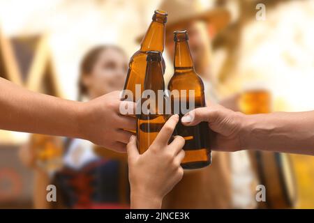Friends clinking bottles with beer during celebration of Octoberfest outdoors Stock Photo