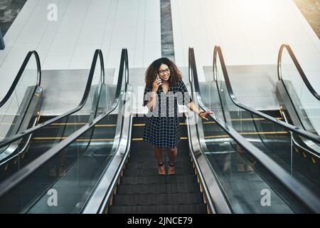 On the move to closing business deals. High angle shot of an attractive young businesswoman taking a phonecall while going up an escalator in a modern Stock Photo