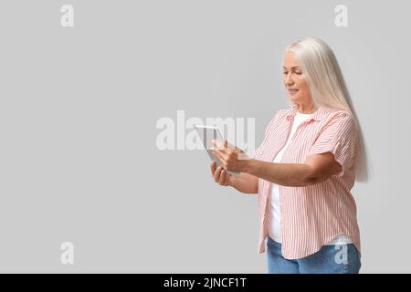 Mature woman using tablet computer for navigation on light background Stock Photo