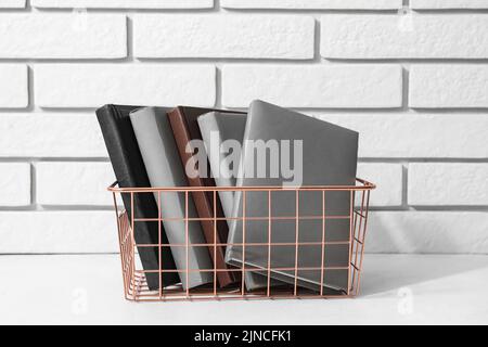 Metal basket with books on table near white brick wall Stock Photo