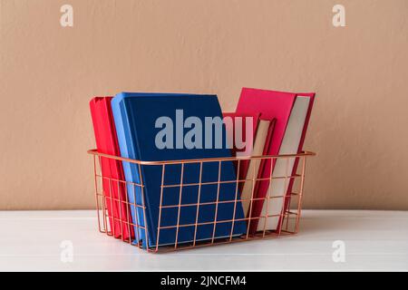 Metal basket with books on table near beige wall Stock Photo