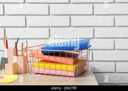 Metal basket with books and pen cups on table near white brick wall Stock Photo