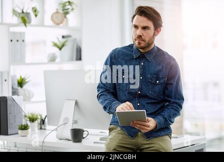 Hes got the right equipment for business. a handsome young businessman looking thoughtful while using a digital tablet in his office. Stock Photo
