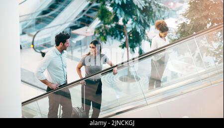 On the way to take a chance at success. two young businesspeople having a chat while going up an escalator in a modern workplace. Stock Photo
