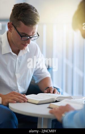 Were seeking for some divine intervention. two young businessmen reading their bibles at work. Stock Photo