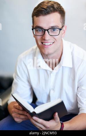 Hes always cheerful after doing some spiritual reading. Portrait of a handsome young businessman reading his bible at work. Stock Photo