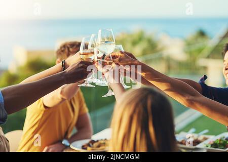 To us growing closer and stronger together. a group of friends raising up their glasses for a toast while sitting around a table together outdoors. Stock Photo