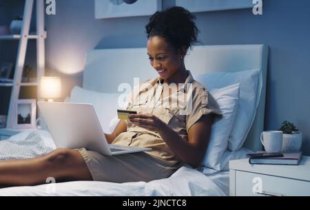 Theres never a bad time to go online shopping. an attractive young woman using her laptop while lying on her bed after a long day at work. Stock Photo