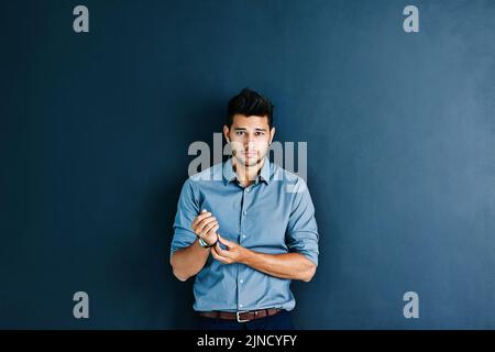 Theres a long way to go but Im ready. Studio portrait of a handsome young businessman adjusting his wristwatch while standing against a grey Stock Photo