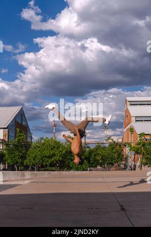 Latino man doing a somersault in mid-air. Hispanic boy doing an extreme flip. Man performing a stunt in the park. Hispanic boy doing an extreme breakd Stock Photo