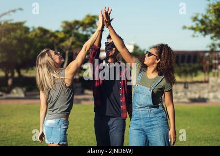 Raising it up high. a group of cheerful young friends giving each other high fives outside in a park. Stock Photo