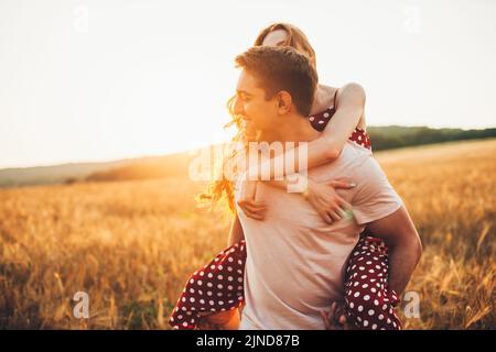 Close-up portrait of a caucasian couple of man and woman walking in an open field, piggy-back ride. Romantic couple dating. Activity relationship. Stock Photo