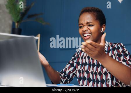 African woman unhappy mad aggressive conflict problem shout looking at laptop. Office employee confused by message of a disgruntled buyer. Stock Photo