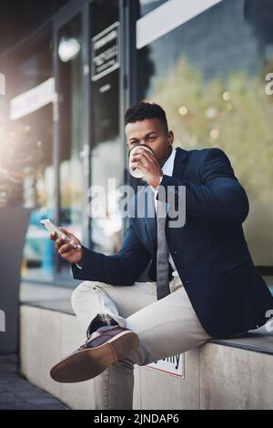 He takes business with him on his breaks. a handsome young businessman using a cellphone while drinking coffee in the city. Stock Photo