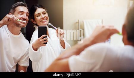 Look at our superstar smiles. a mature couple taking selfies while brushing their teeth in the bathroom at home. Stock Photo