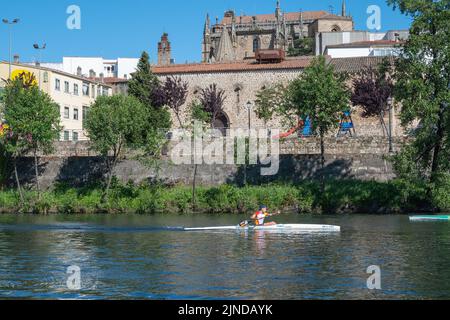 Plasencia, Spain - April 17, 2021: A young man practices canoeing riding in his canoe navigating the Jerte river and the cathedral in the background Stock Photo