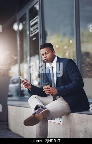 Catching some connectivity during his free time. a handsome young businessman using a cellphone while drinking coffee in the city. Stock Photo