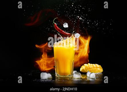Mangonada Mexican mango smoothie with chamomile sauce and chili lime spice. Mango and chili pepper cocktail on a black background. Ice cubes fall into Stock Photo
