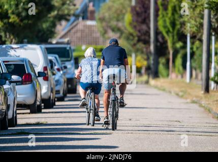 Rear view of a pair of senior cyclists, male & female, riding in the road together on a warm day in Summer, UK. Stock Photo