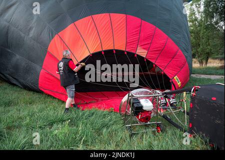 Heldburg, Germany. 11th Aug, 2022. A pilot prepares his hot air balloon for takeoff for the 1st flight of the German Hot Air Ballooning Championship. The 25th Thuringian Montgolfiade, the German Hot Air Ballooning Championship, takes place for the first time in Heldburg. Of the 58 hot air balloons registered, 33 will take part in the competition. The organizer is the Ballonsportclub Thüringen. The Montgolfiade offers a hiking program on the weekeine together with the tourism association Coburg-Rennsteig. Credit: Daniel Vogl/dpa/Alamy Live News Stock Photo